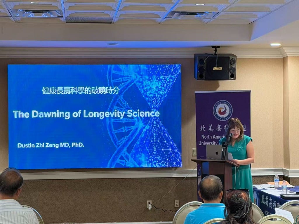Presenter at the podium beside a screen titled The Dawning of Longevity Science at Hilton San Gabriel